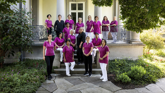 17 Frauen des Hotellerie-Service-Teams der Klinik Meissenberg stehen in Arbeitskleidung auf und vor einer Terrasse